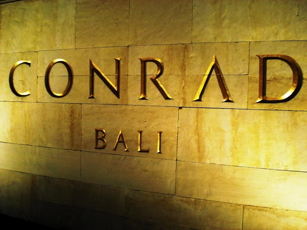 Illuminated Conrad Bali lettering on a stone wall.