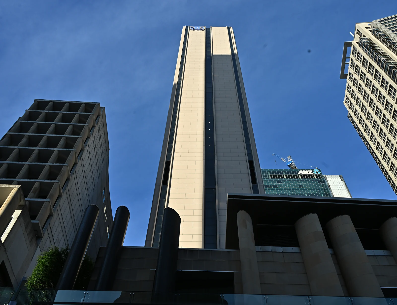 Hilton Sydney tower rising above its street-level entrance against a blue sky.