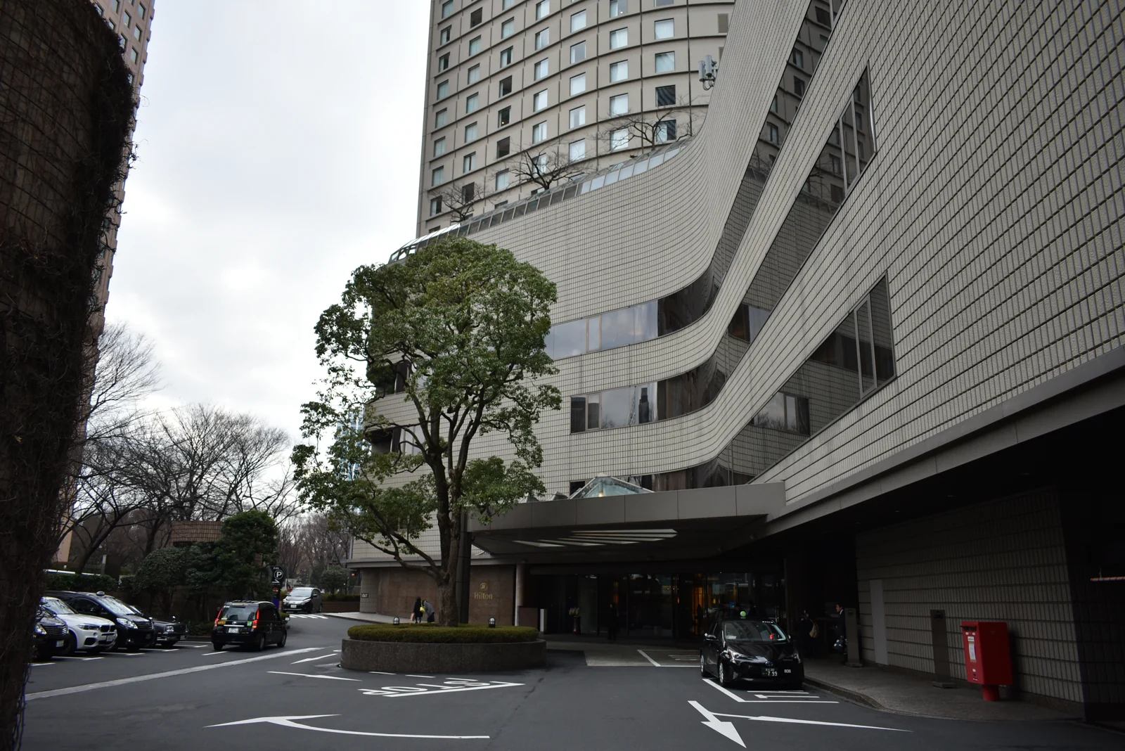 Driveway and covered entrance beneath the curved facade of Hilton Tokyo.