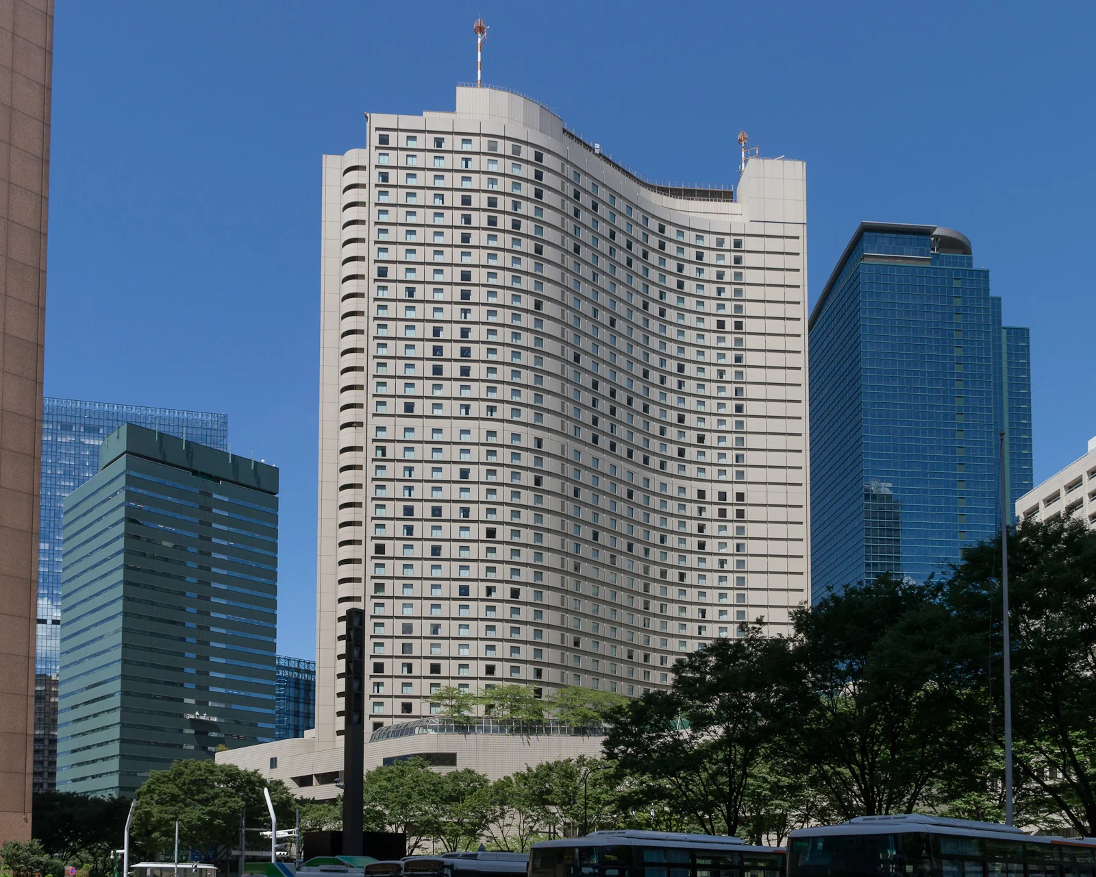 Curved Hilton Tokyo tower in Shinjuku with trees and nearby office buildings.